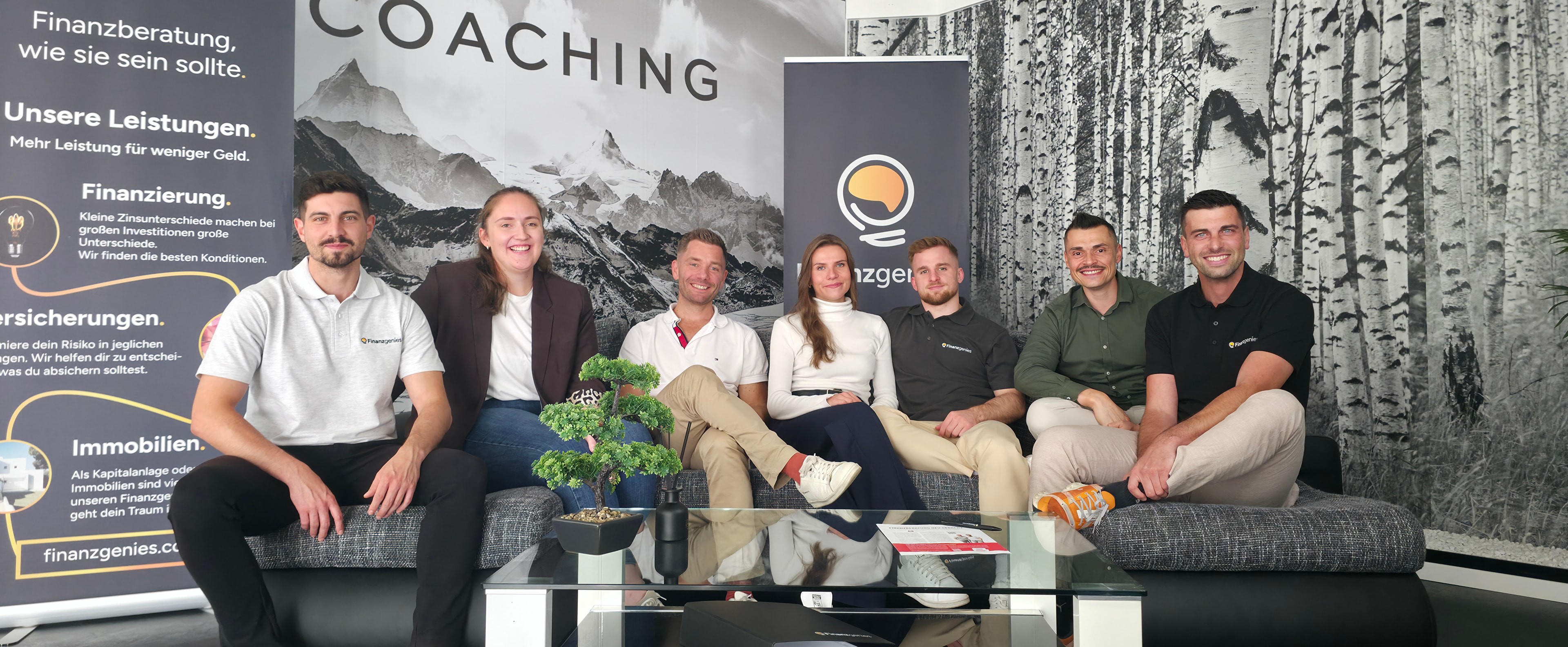 Finanzgenies Team gemeinsam auf dem Sofa vor Markenbannern und Büro-Wandgestaltung